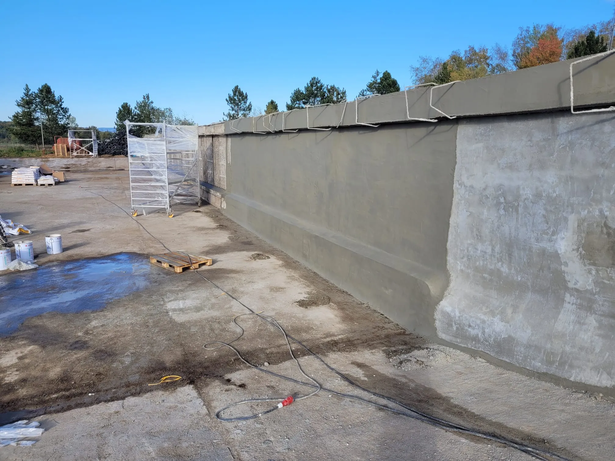 Construction site showing a partially repaired concrete wall with fresh cement patching under a clear blue sky.