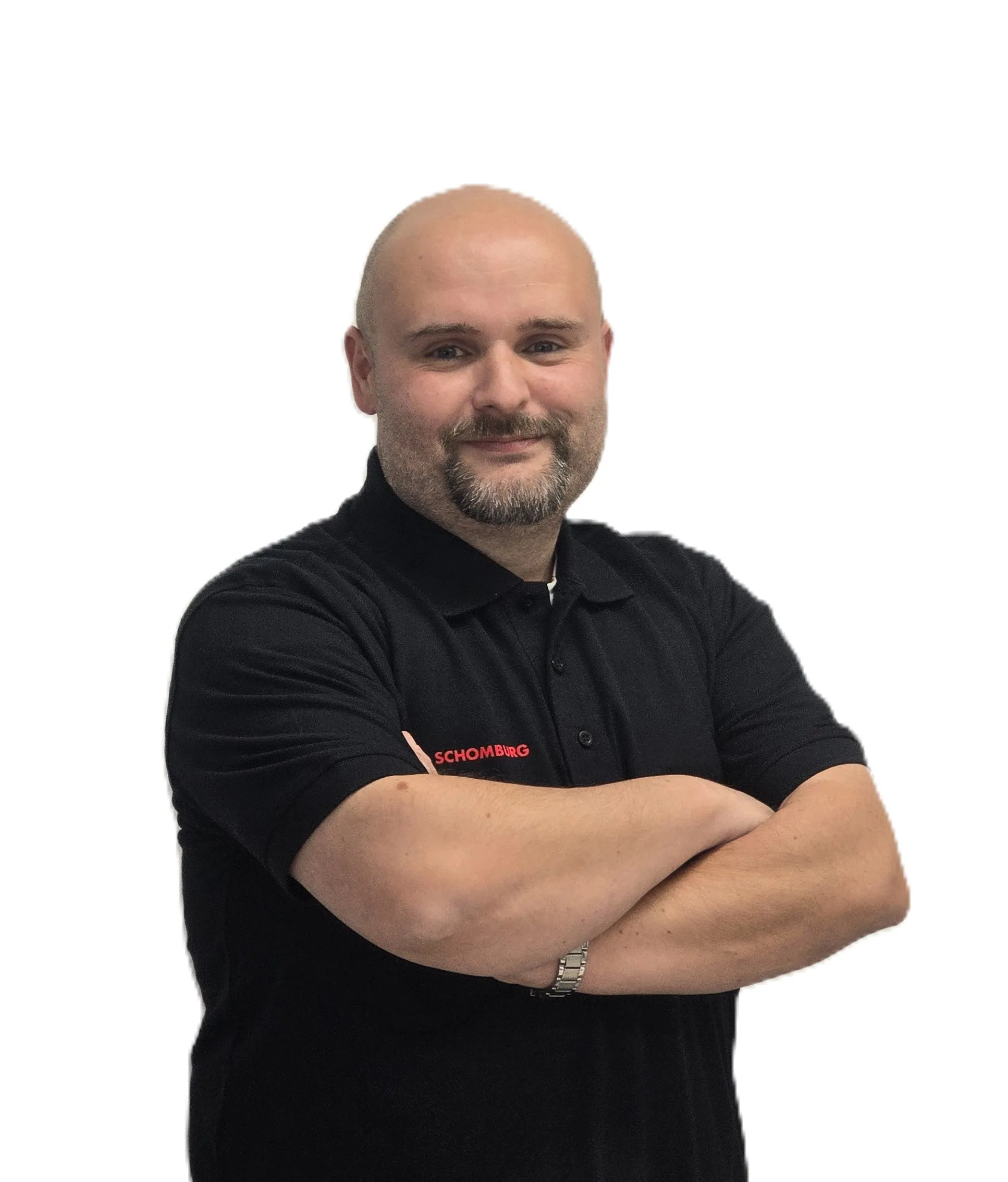 Smiling bald man with a beard wearing a black SCHOMBURG polo shirt with arms crossed.