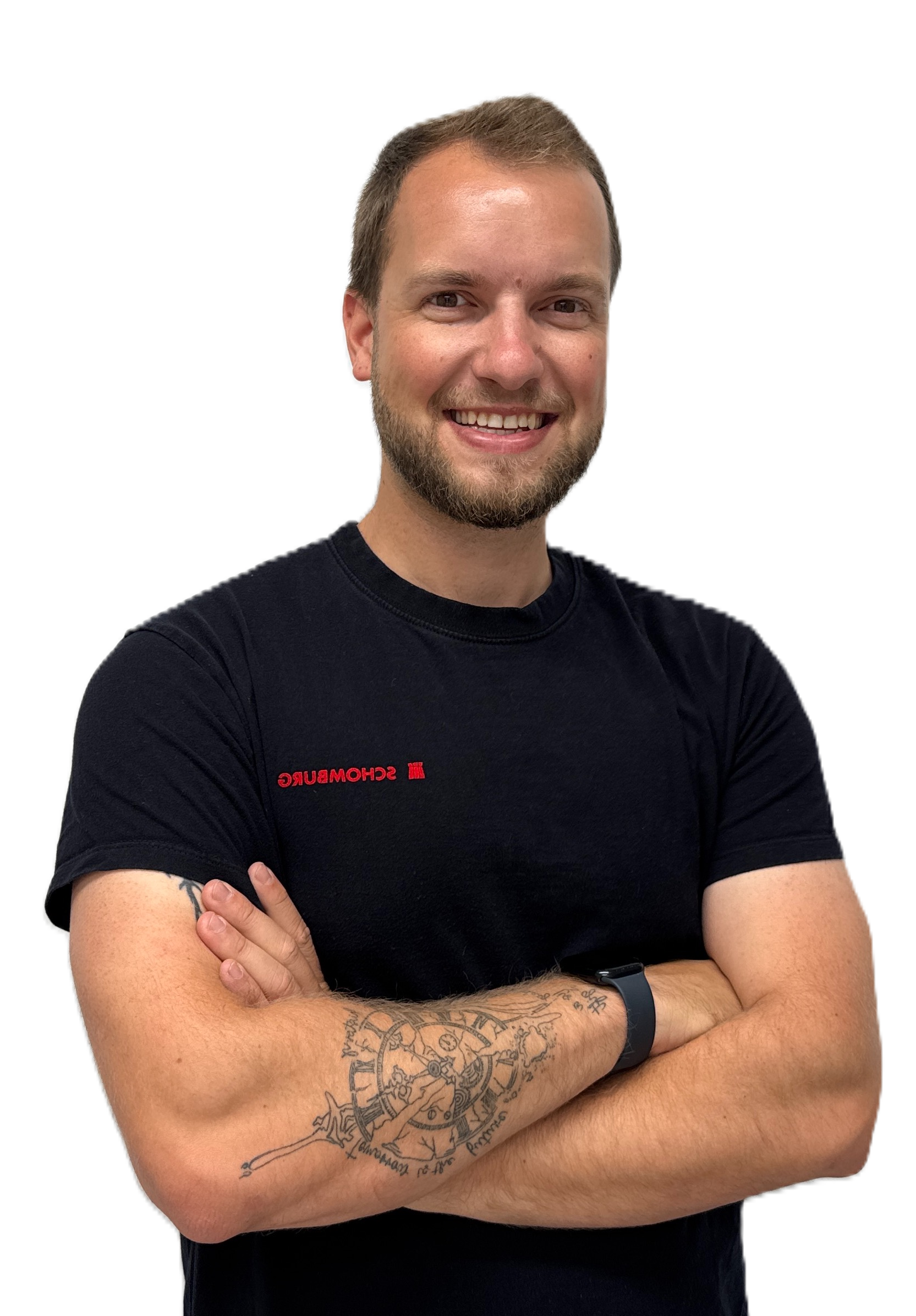 Smiling man with short hair and beard wearing a black Schomburg T-shirt and a smartwatch, with a detailed clock tattoo on his forearm.