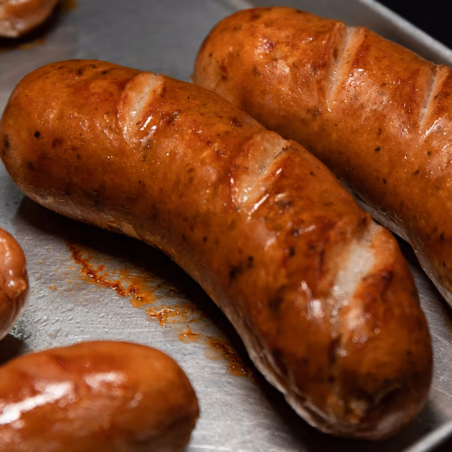 Close-up of browned, grilled sausages with glistening skin and slight char marks on a metal tray.