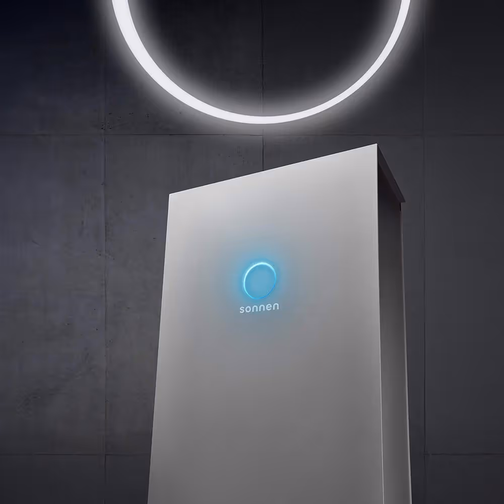 sonnenBatterie mit leuchtendem blauen Logo in einem Raum mit dunkler Wand und leuchtendem Lichtkreis.