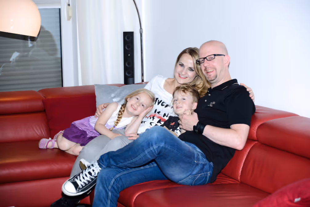 Mutter, Vater Tochter und Sohn auf dem roten Sofa in Ihrem Haus mit Solaranlage und Solarspeicher