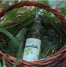 Flasche Sonnenliebe Limonade inmitten von grünen Tannenzweigen in einem Korb.