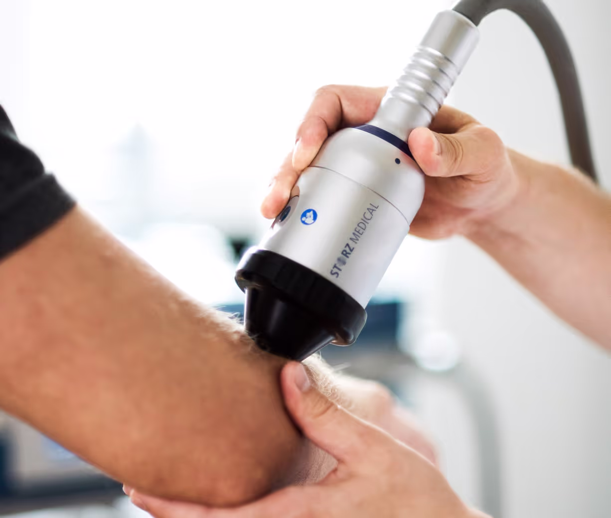 Ärztliche Behandlung am Ellenbogen eines Patienten in einer orthopädischen Praxis.