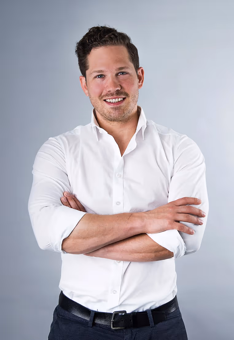 Porträt von Dr. Philipp Reb, lächelnd, im Anzug vor neutralem Hintergrund.