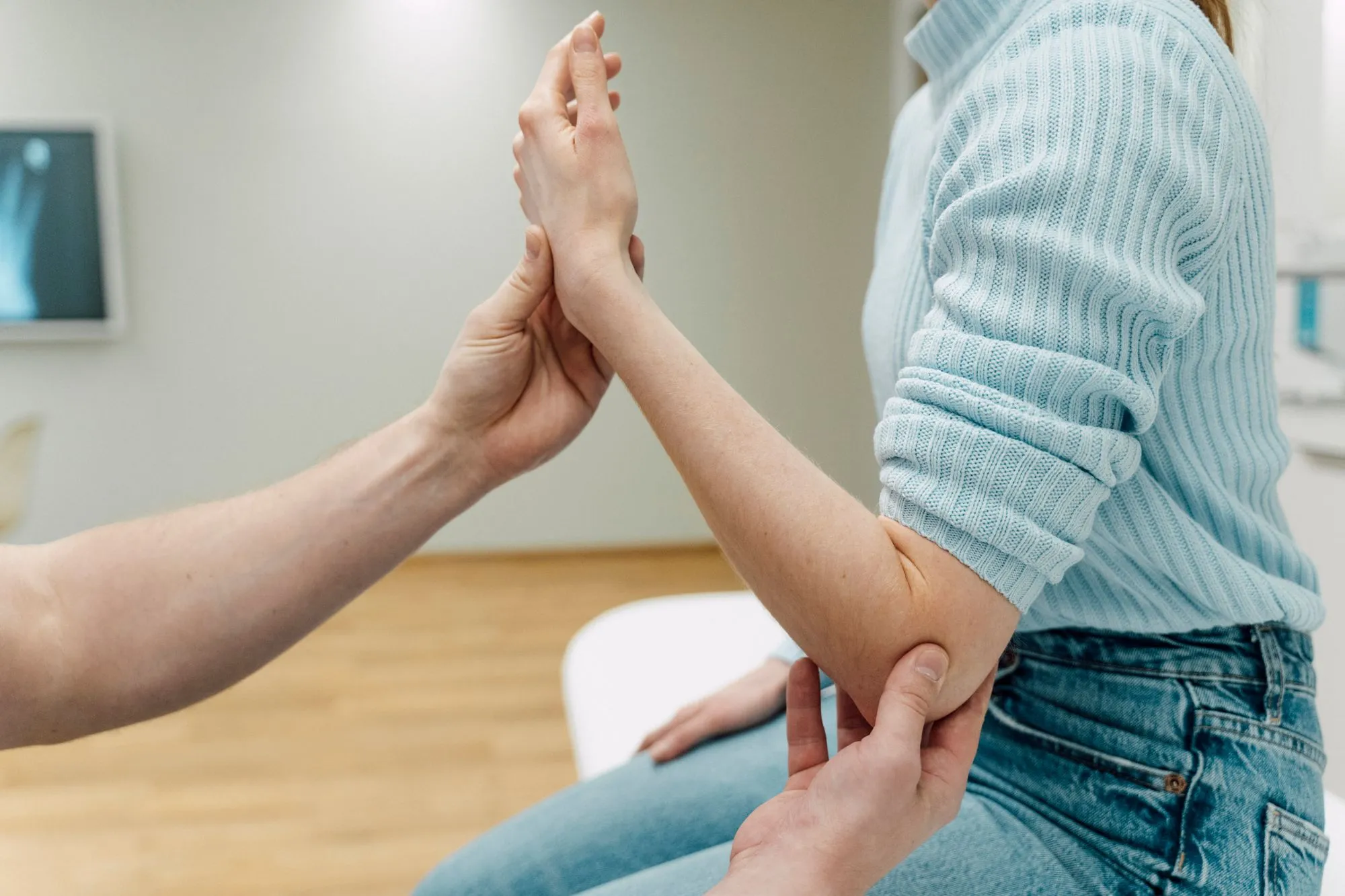 Ärztliche Behandlung am Ellenbogen eines Patienten in einer orthopädischen Praxis.