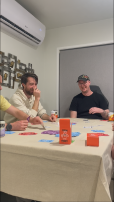 Four guys playing cockfight around a table.