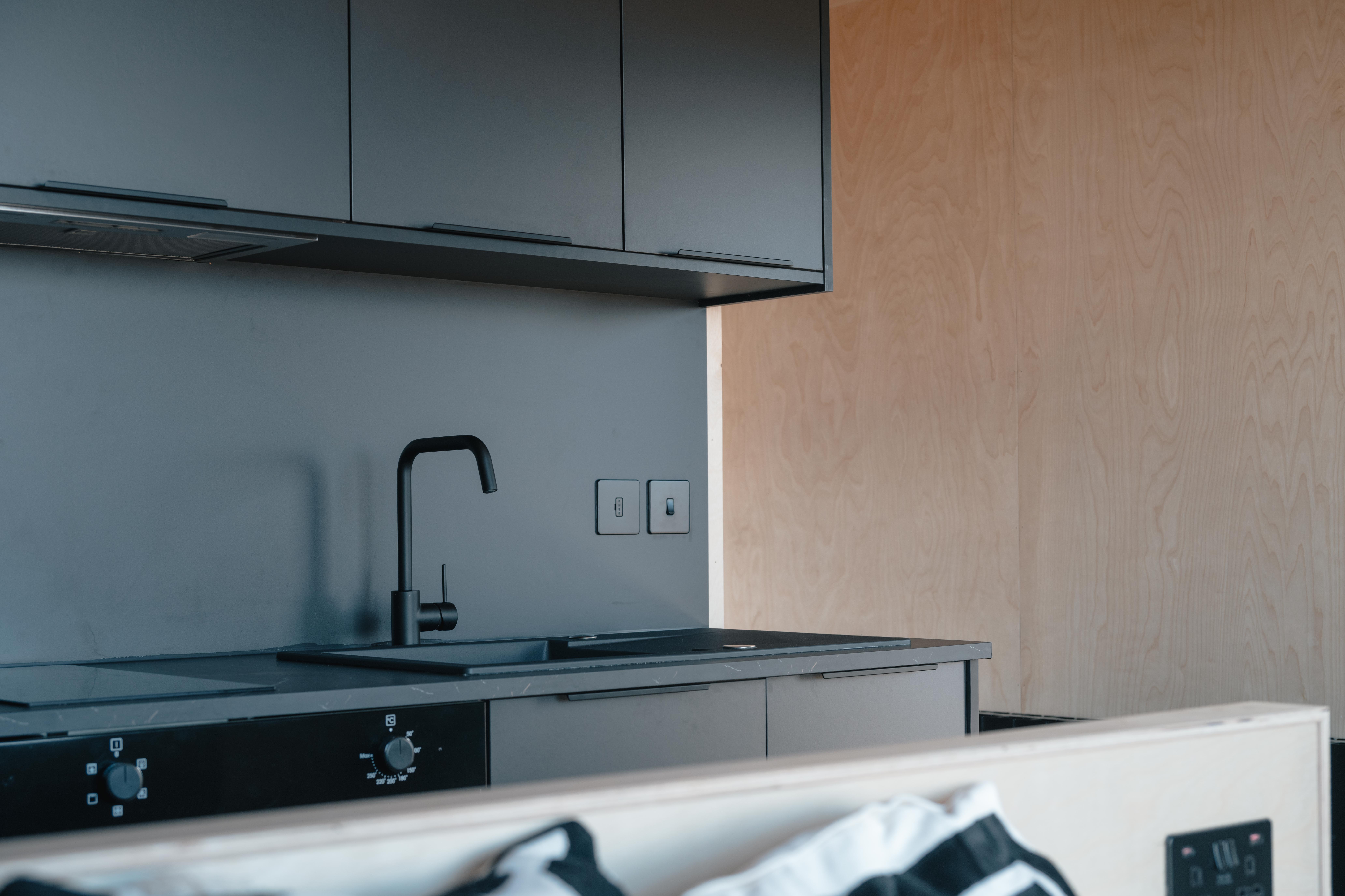 Modern kitchen countertop with black electric stovetop, coffee maker, kettle, sink, and matte black cabinets.