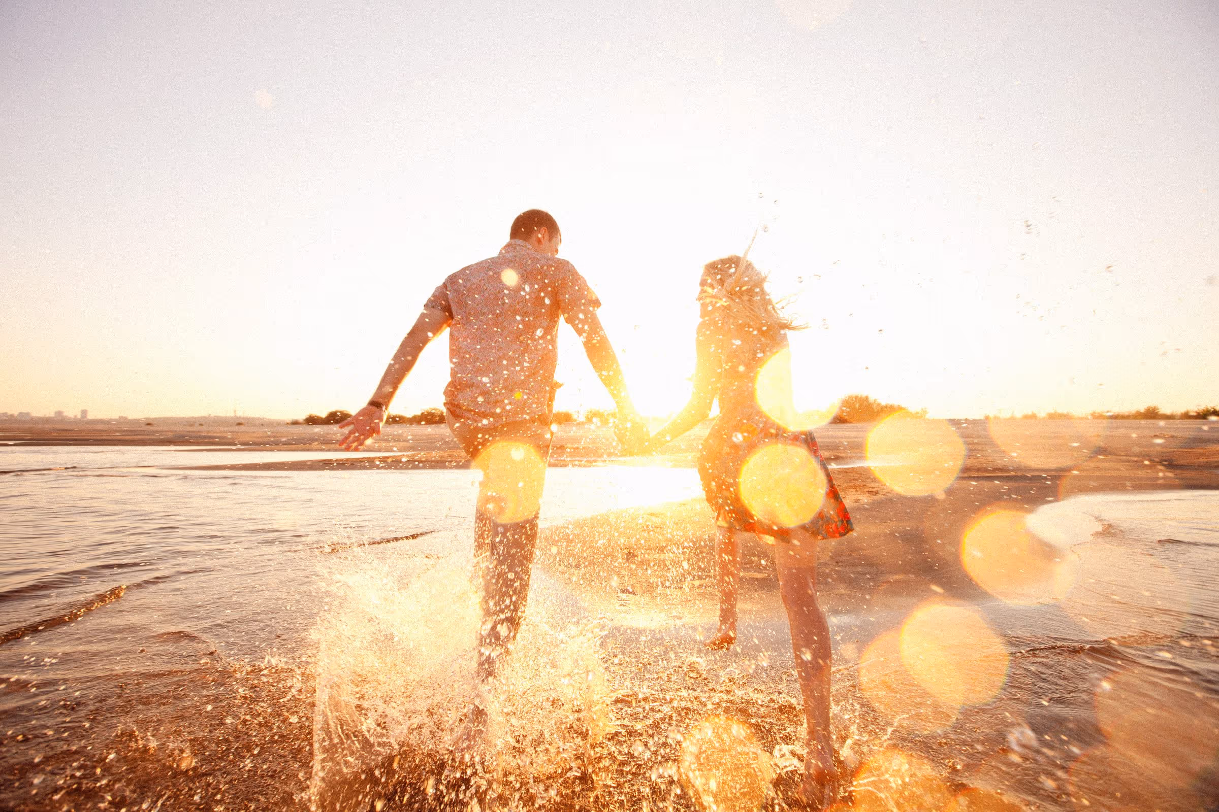 Couple running through the water on a beach at sunset