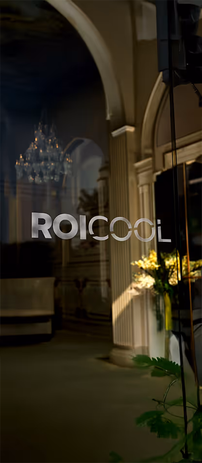 Cam kapı üzerinde ROICOOL yazan logo ve iç mekanda sarkan bir avize ile çiçekler.