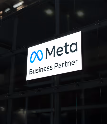 Meta Business Partner yazan ve Meta logosu bulunan bir tabela, cam bir cephe önünde asılı durumda.