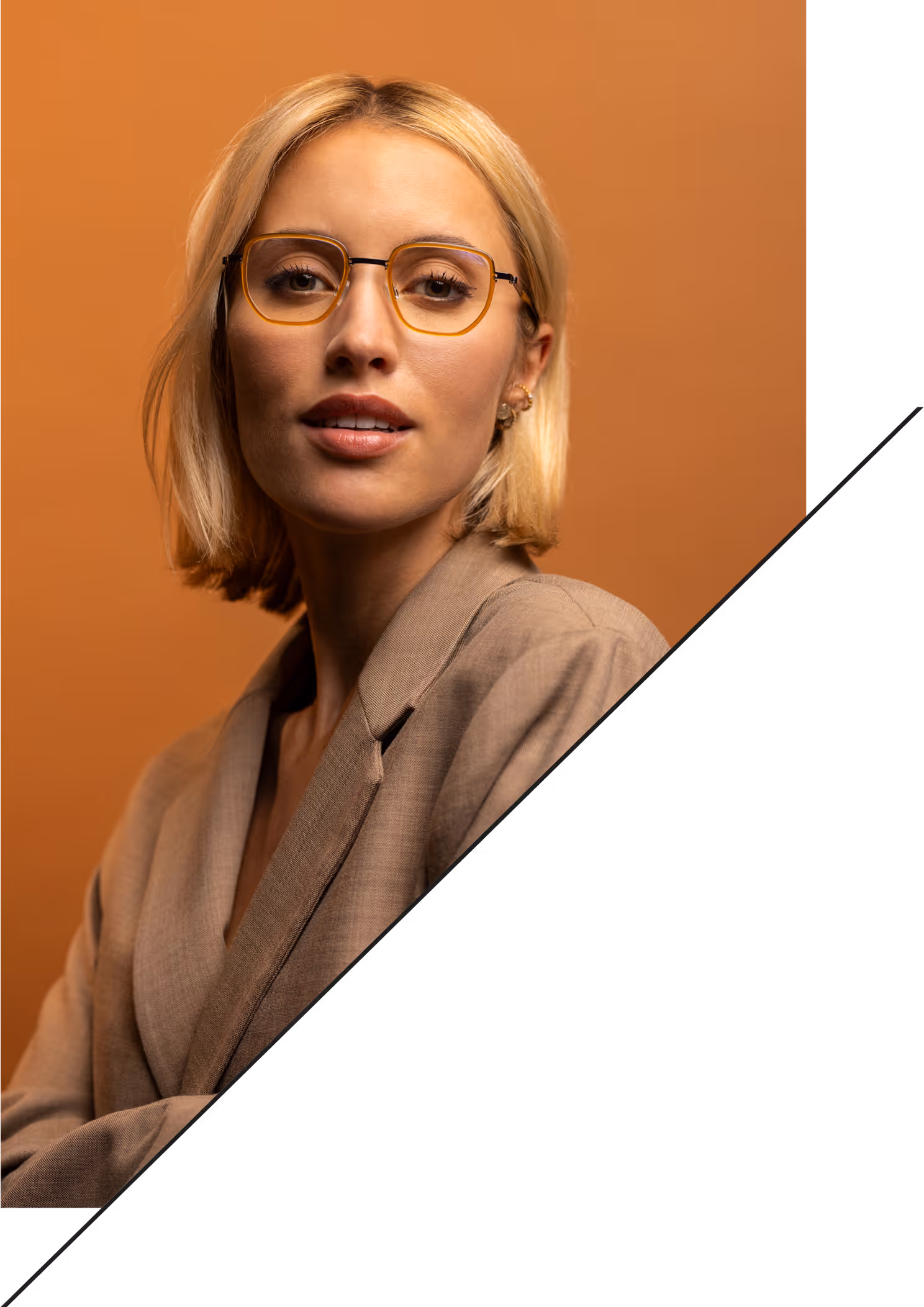 Ein blondes Model mit halblangen Haaren steht lächelnd vor einem orangefarbenen Hintergrund. Sie trägt einen modischen Blazer und eine orangefarbene Brille von Feinleicht, die farblich auf das Gesamtbild abgestimmt ist.
