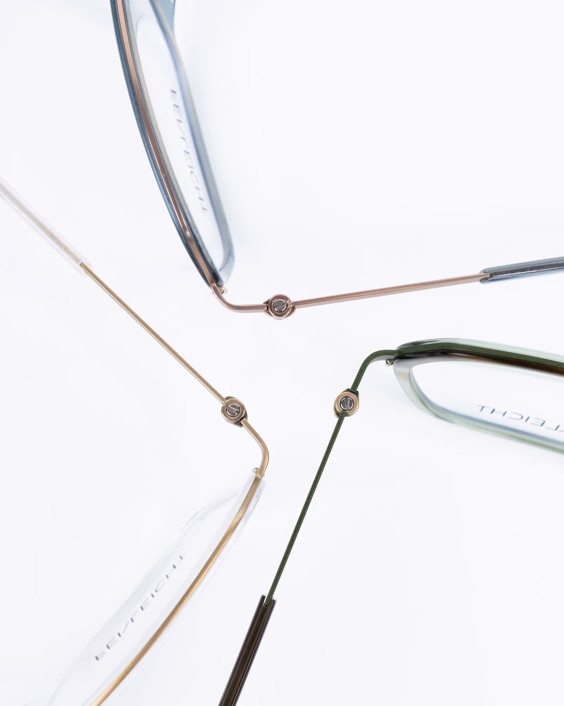 Drei stilvoll angeordnete Feinleicht Brillen in Gold, Grün und Rosé mit hellblauen Bio-Acetat-Details – modernes Farbspiel in dynamischer Komposition.