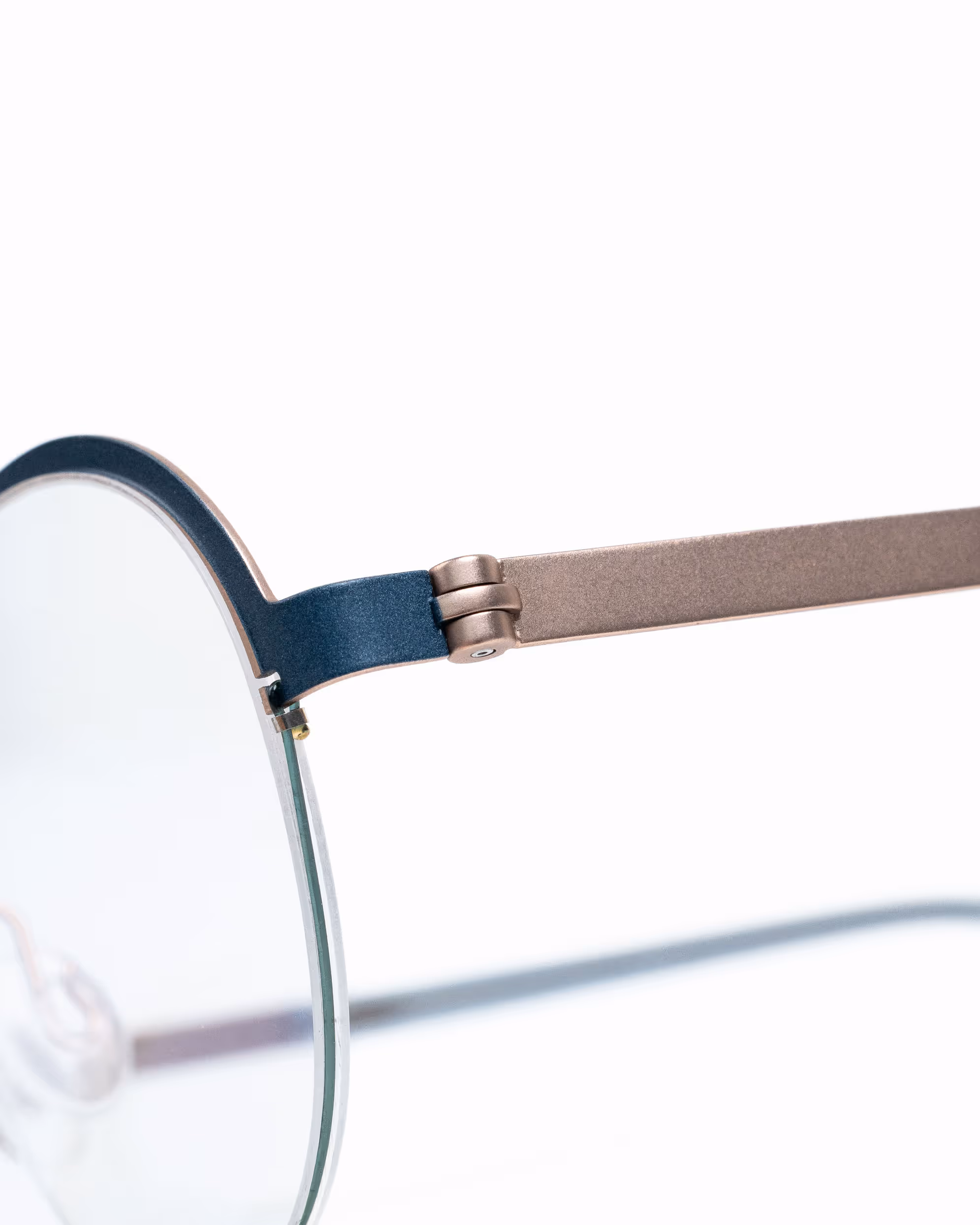 Detailansicht des Scharniers einer Feinleicht Fassung aus mattiertem Titan in Rosé mit fein gesetzten dunkelblauen Farbdetails.