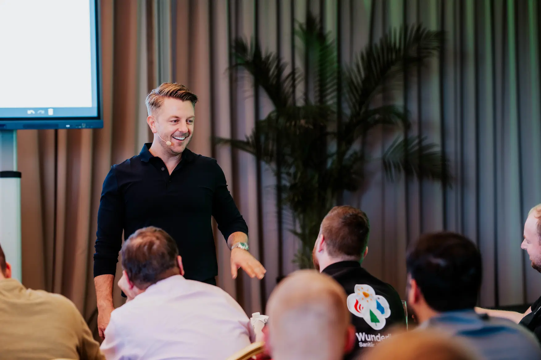 Matthias Aumann mit Mikrofon vor Publikum bei Präsentation in einem Konferenzraum.