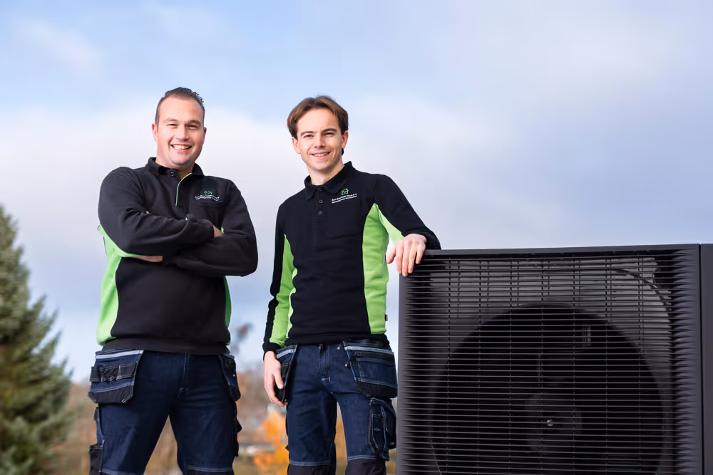 Jeroen en Niels van Eenduurzaamthuis trots naast een zwarte warmtepomp die zij in Zwolle hebben geinstalleerd