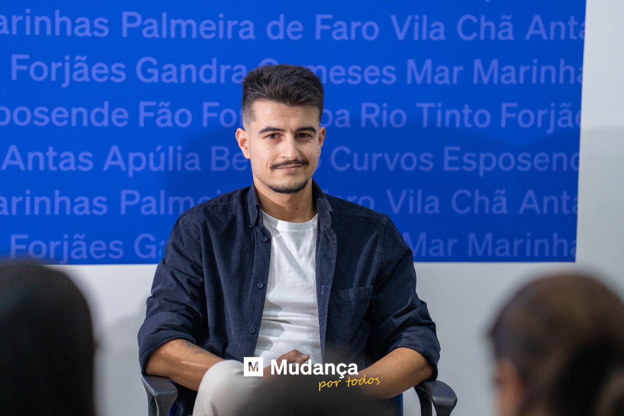 Pode ser uma imagem de 2 pessoas, sala de imprensa e a texto que diz "Fão ApúliaB Marinh Tinto Forja CurvosEsposen M Mudança portodos por todos"