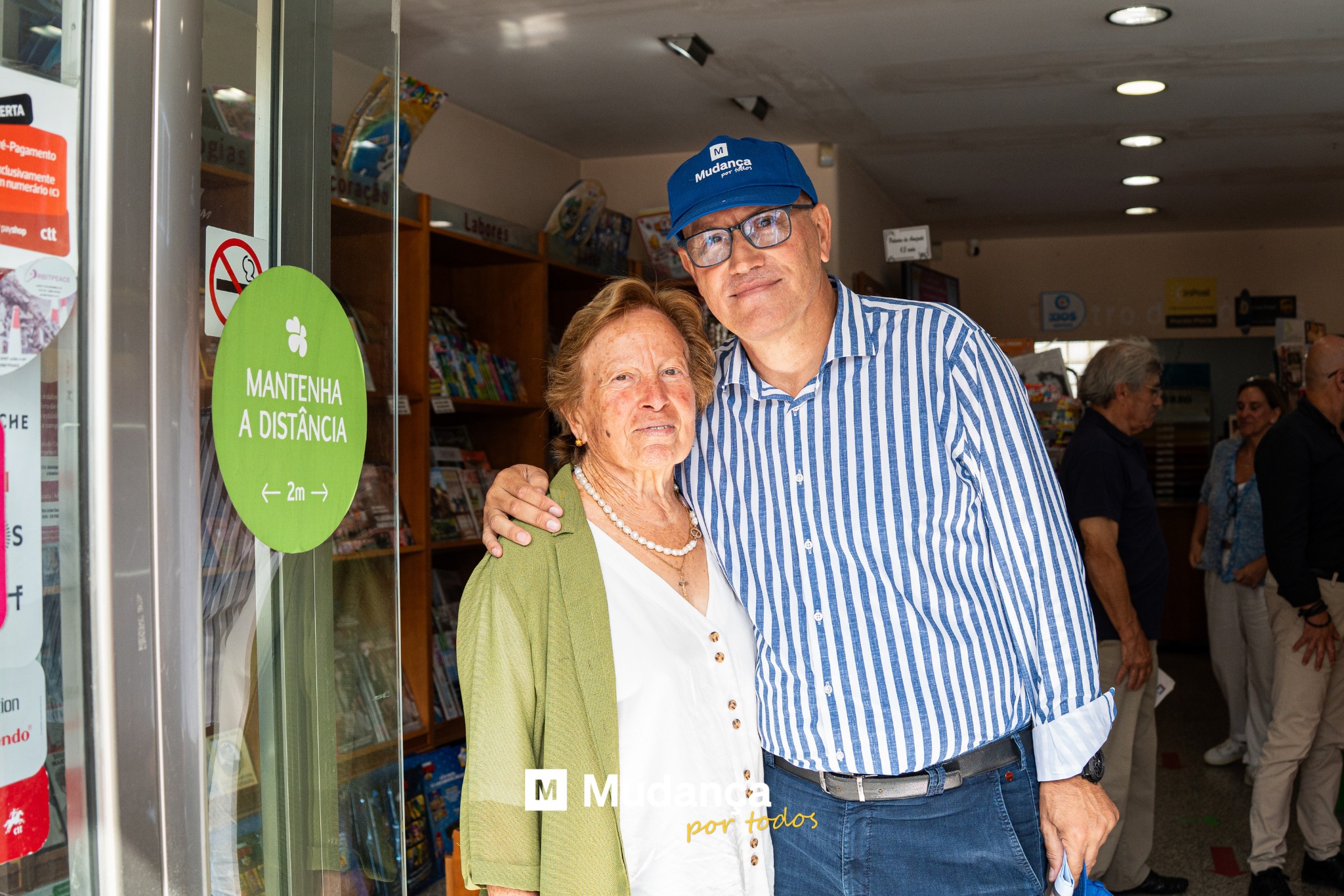 Pode ser uma imagem de 4 pessoas, pessoas a sorrir, banca de jornais e a texto que diz "ERTA Fegamento Shamert fumerárioio Mudanga mộ Sa HE MANTENHA A ADISTÂNCIA S ←2m→ on ndo MM MMedanca M Midanca dlano M por portodos todos"