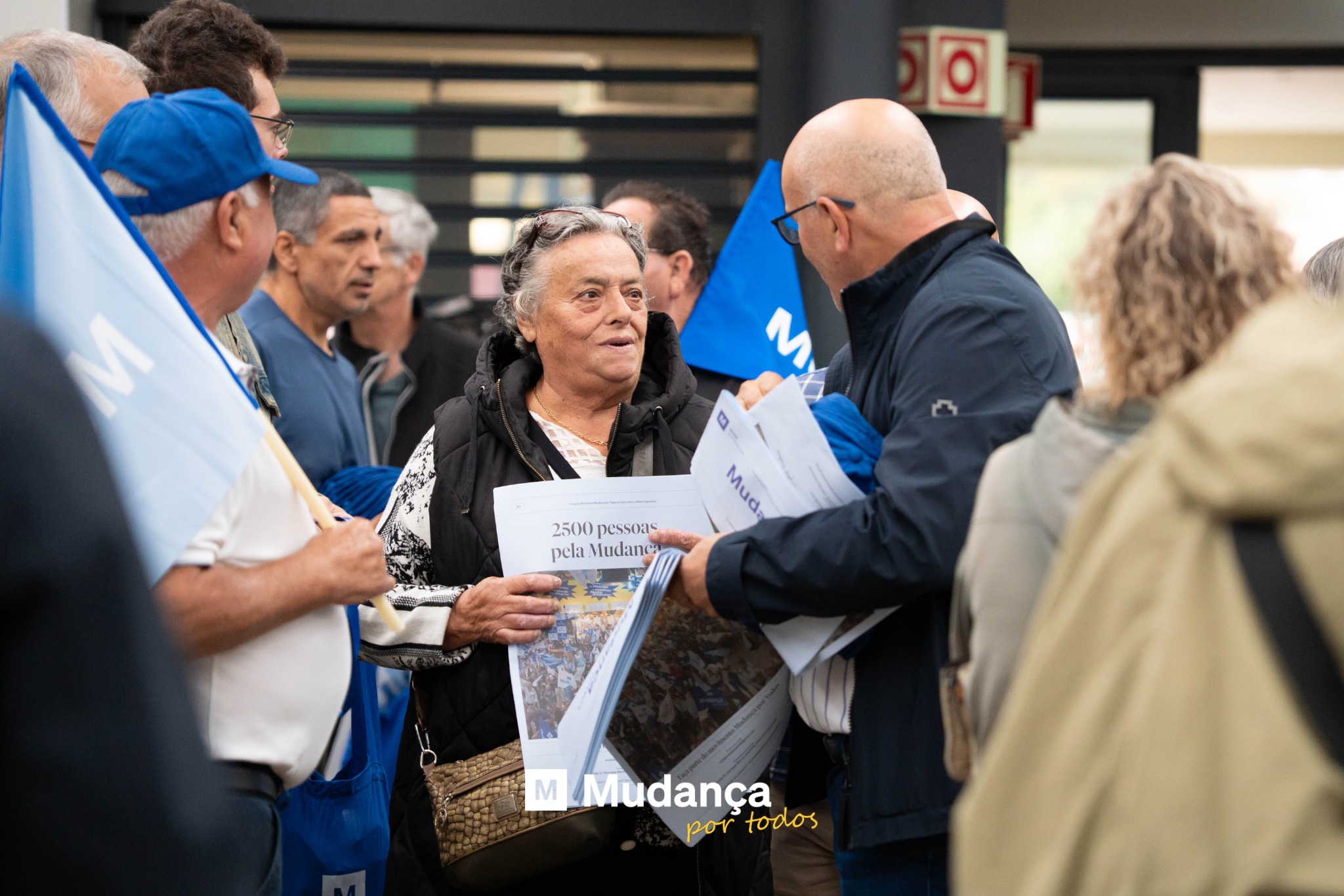 Pode ser uma imagem de ‎4 pessoas, multidão e a ‎texto que diz "‎0 Mud: 2500pessoas 2500 pelaNiudanes pessoas pela Mudanc ビ生 هکمفاتة؟ M Mudança portodos por todos‎"‎‎