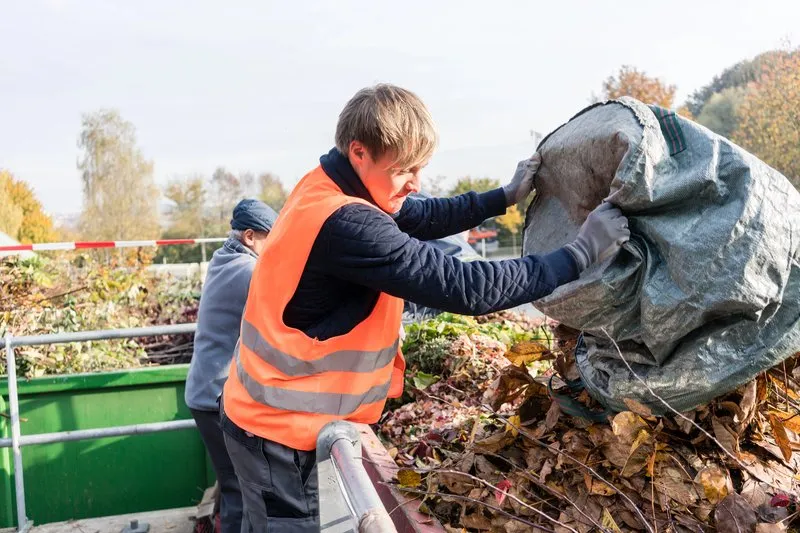 Employé d’une entreprise de débarras vidant un sac de déchets végétaux dans une benne à compost.