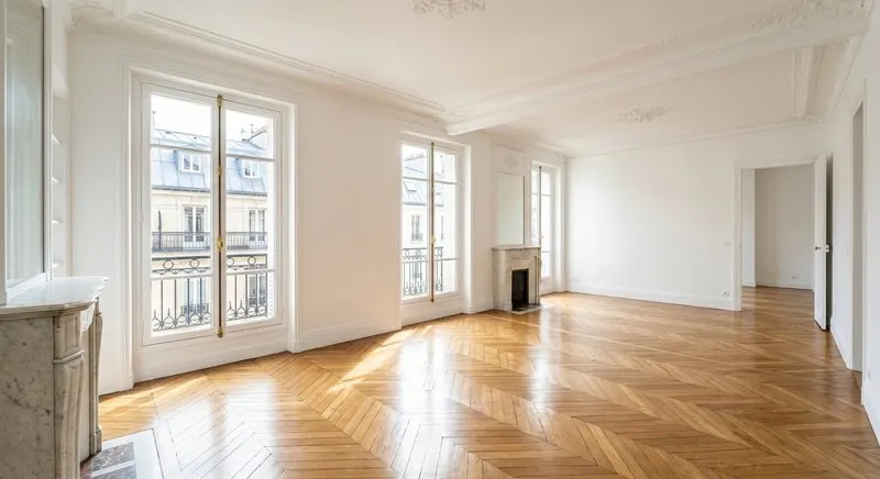 Salon haussmannien vide avec parquet point de Hongrie et cheminée en marbre après un débarras complet