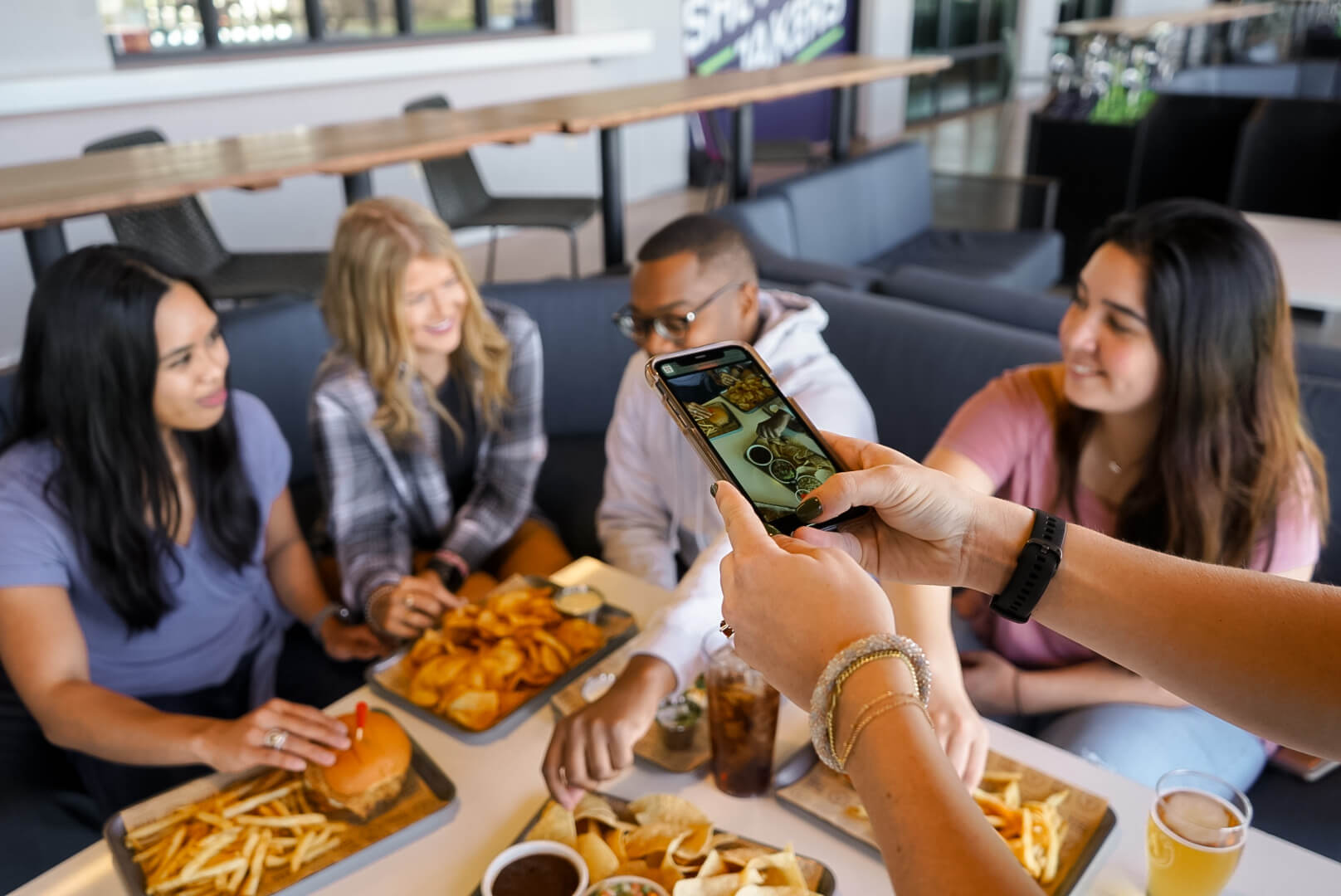 Friends sit around a table enjoying food while someone snaps a photo of the meal.