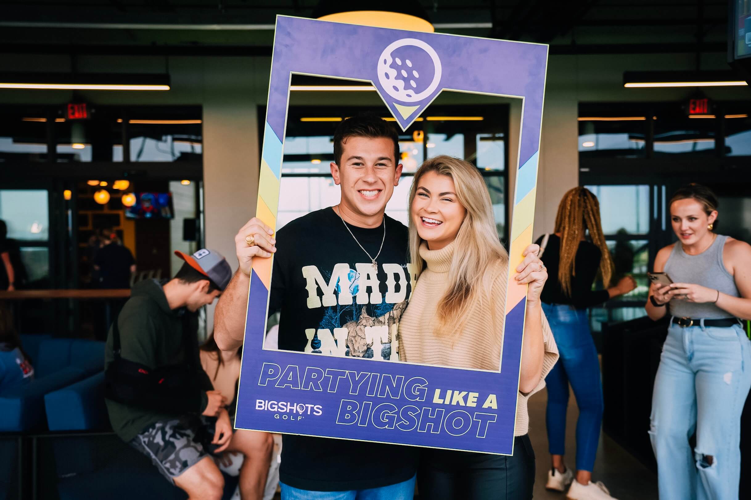 Two people smiling and posing with a "Partying Like a Bigshot" photo frame.