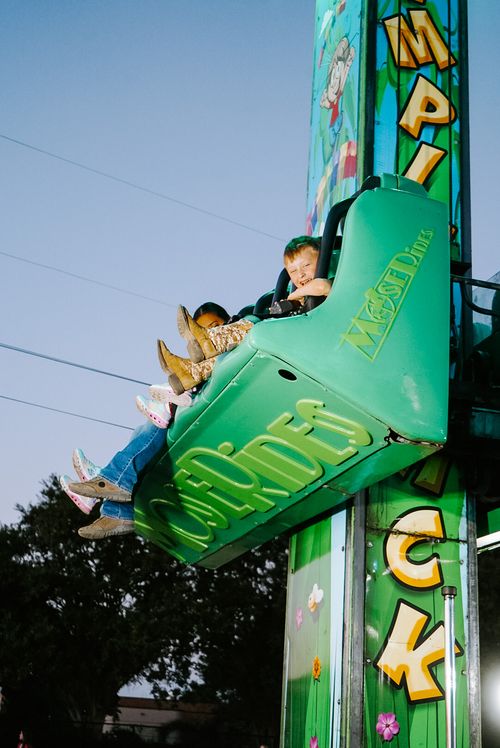 Kids on a green drop ride, legs dangling and smiling with excitement.