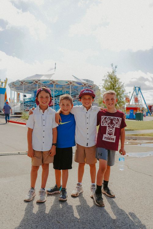 Four young boys smile and pose together at an amusement park.