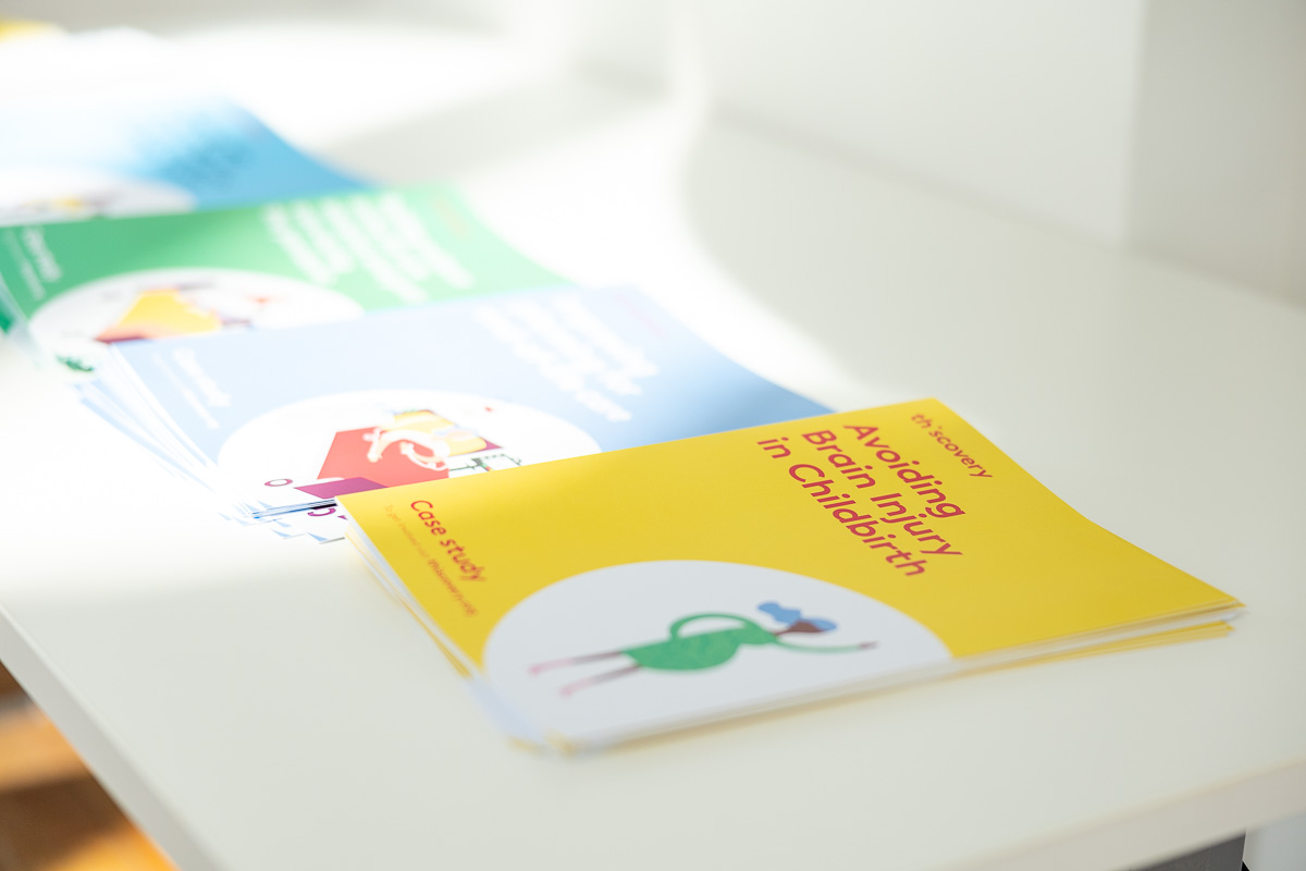 Thiscovery case study brochures displayed on a table with the focus on a yellow one titled: 'Avoiding Brain Injury in Childbirth'.
