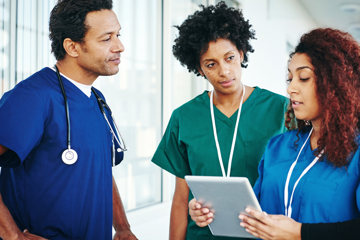 A group of three healthcare professionals discussing a digital tablet.