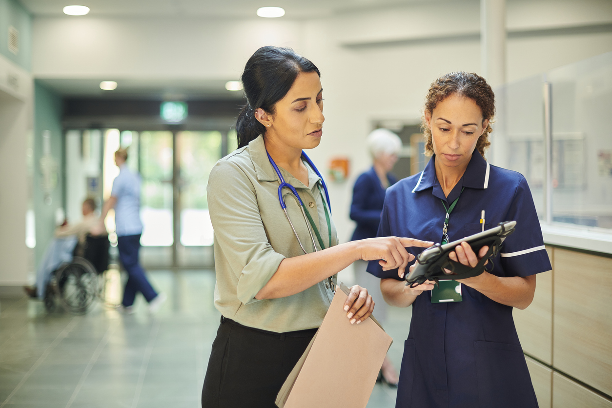 Staff nurse consulting a ward doctor about information on a medical record database using a tablet.