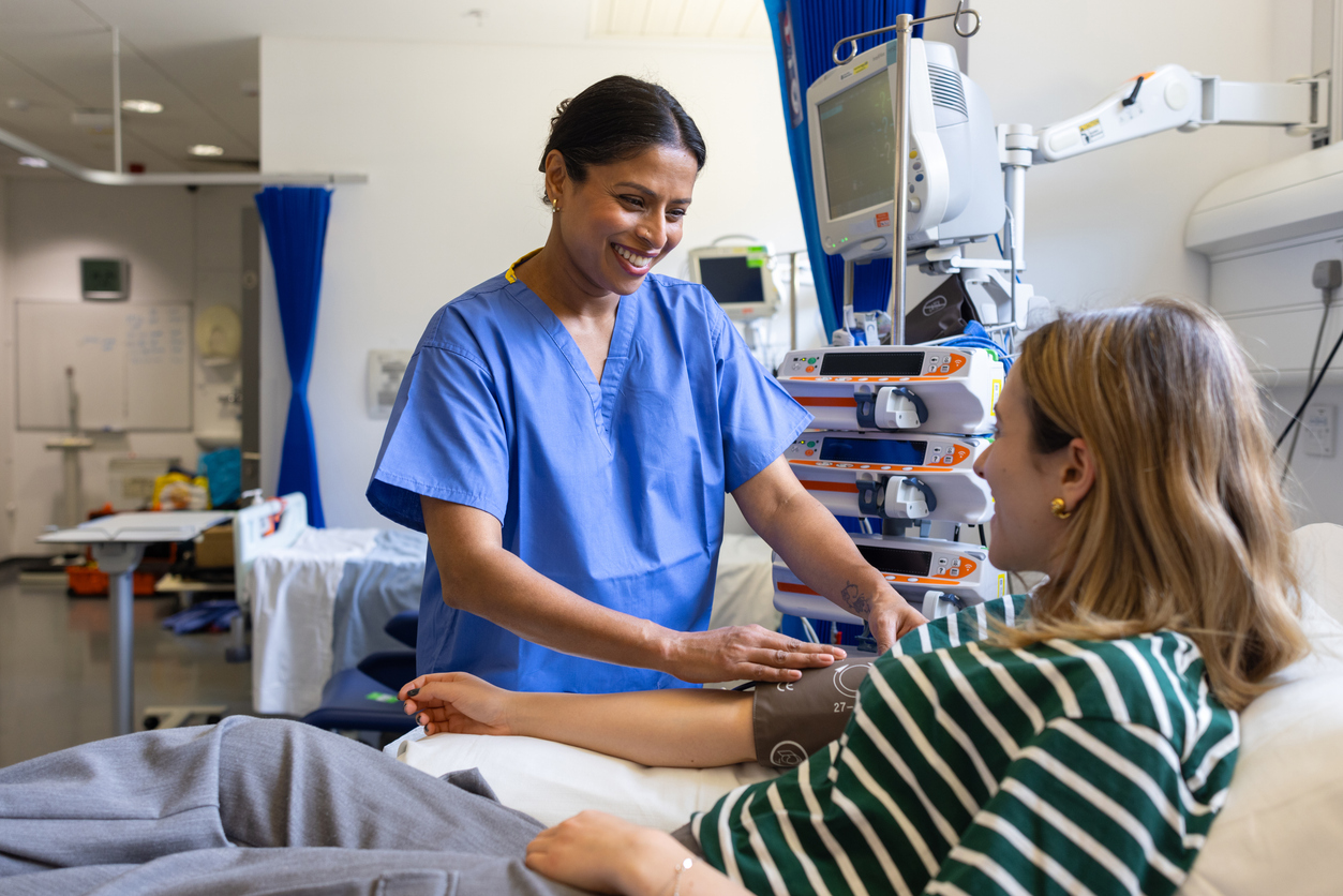 A young female in-patient sitting on a hospital bed and talking to a nurse while she has her blood pressure measured.