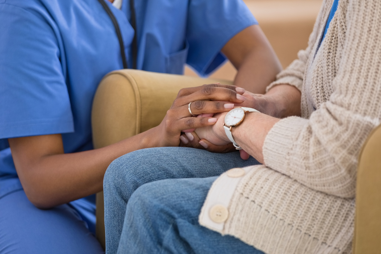 A patient holds hands with a nurse wearing blue scrubs.
