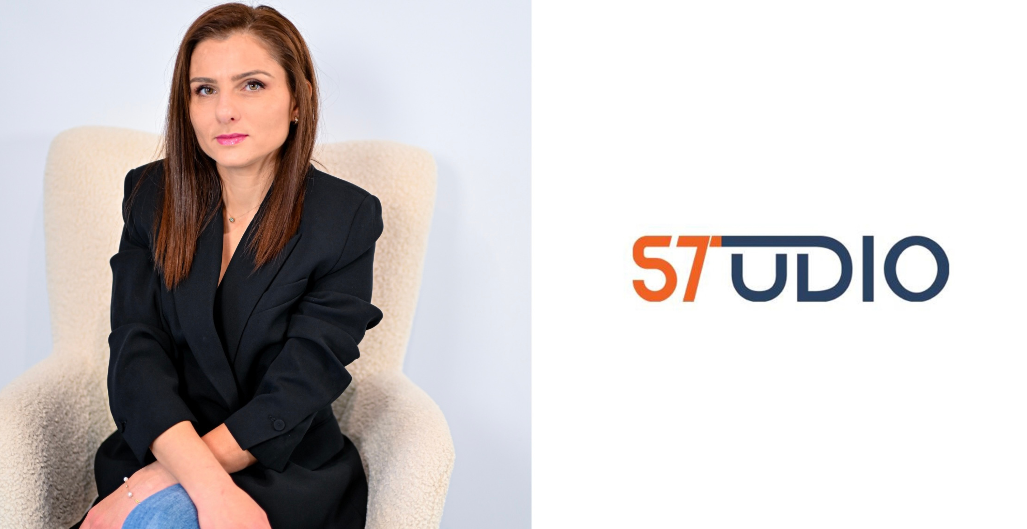 Woman with straight brown hair wearing a black blazer and blue jeans sitting on a beige textured armchair beside the orange and blue S7 Studio logo on a white background.