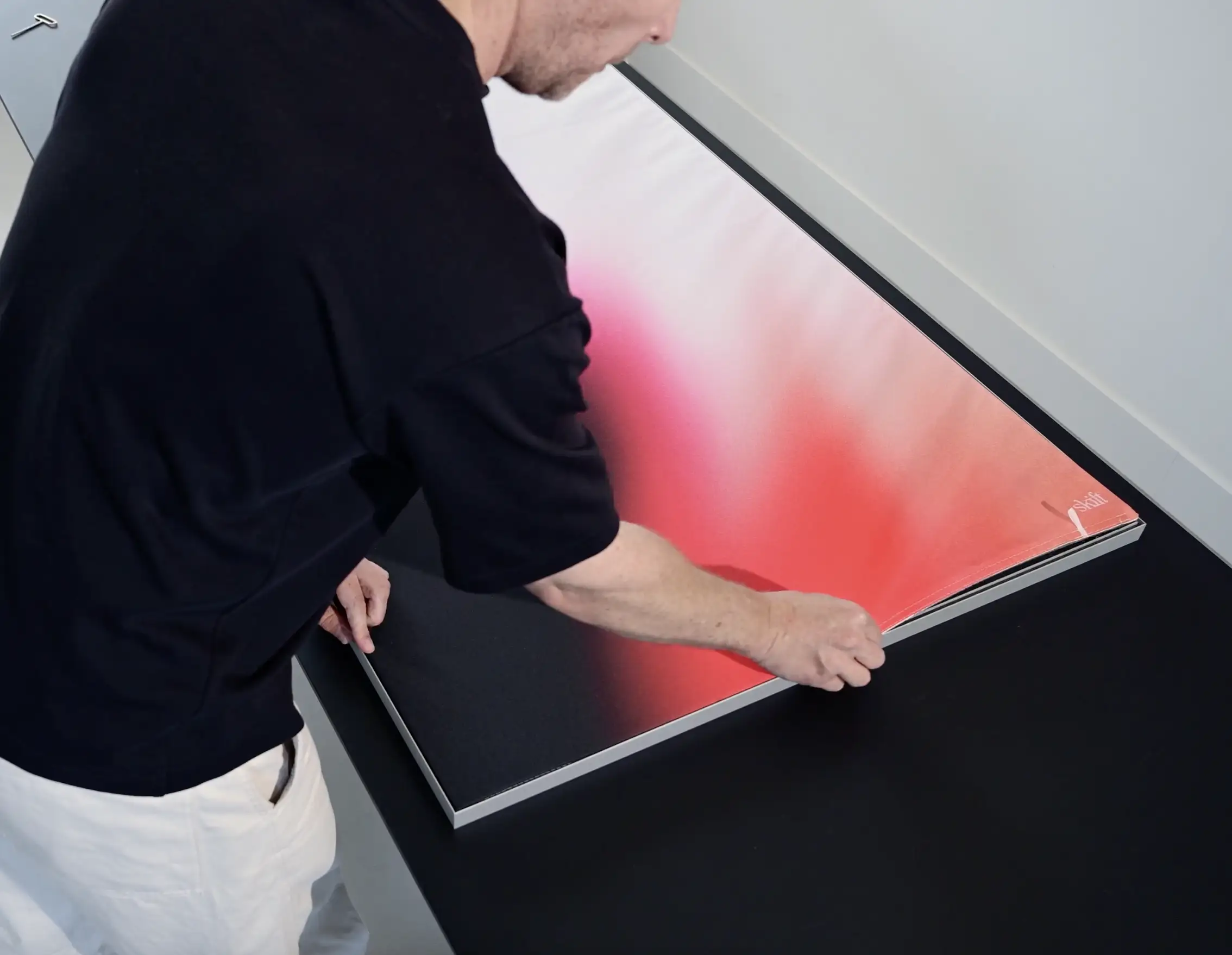 Person lifting the corner of a large framed print with a gradient design from red to white.