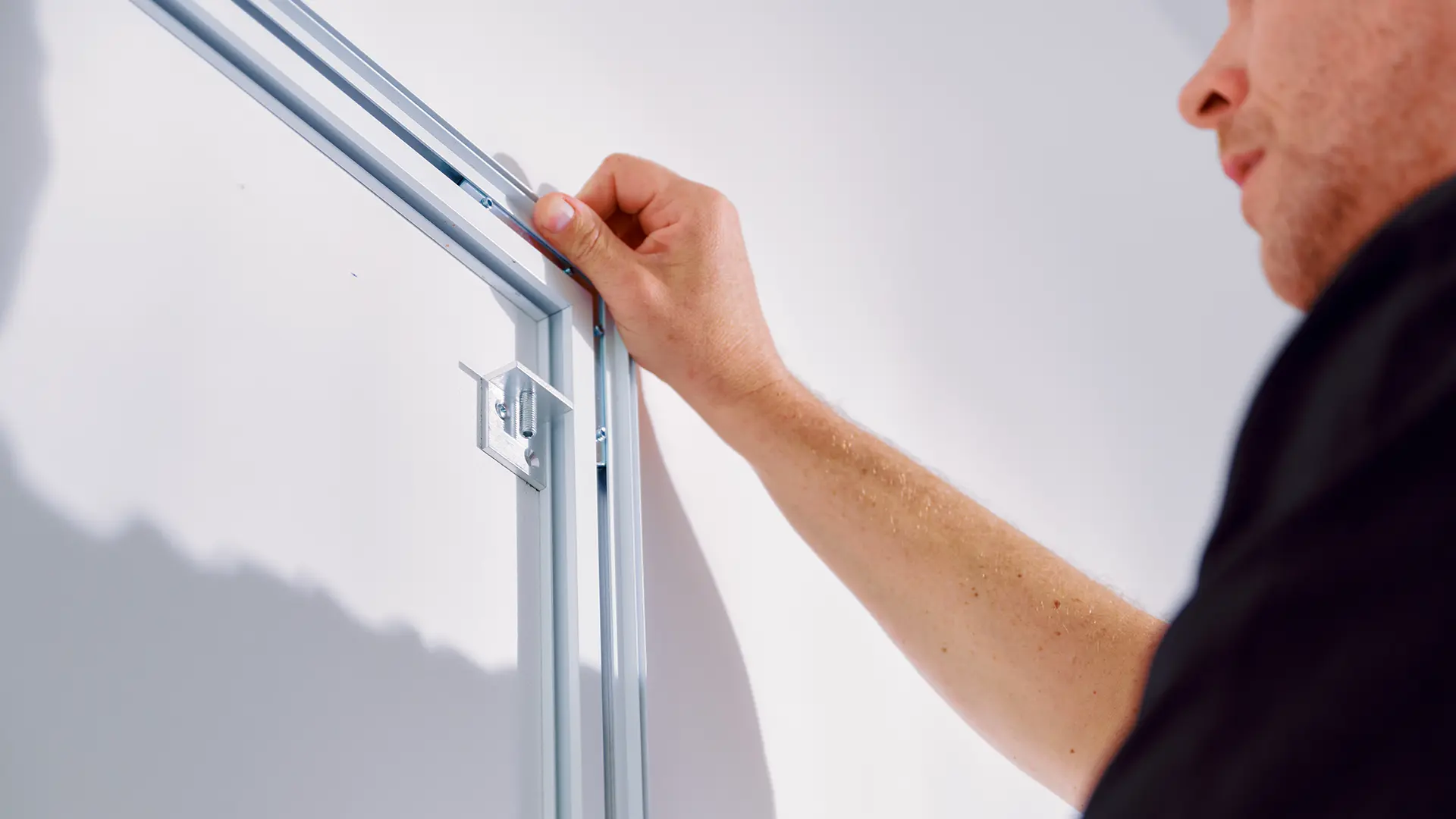Man installing or adjusting a metal door frame against a white wall.