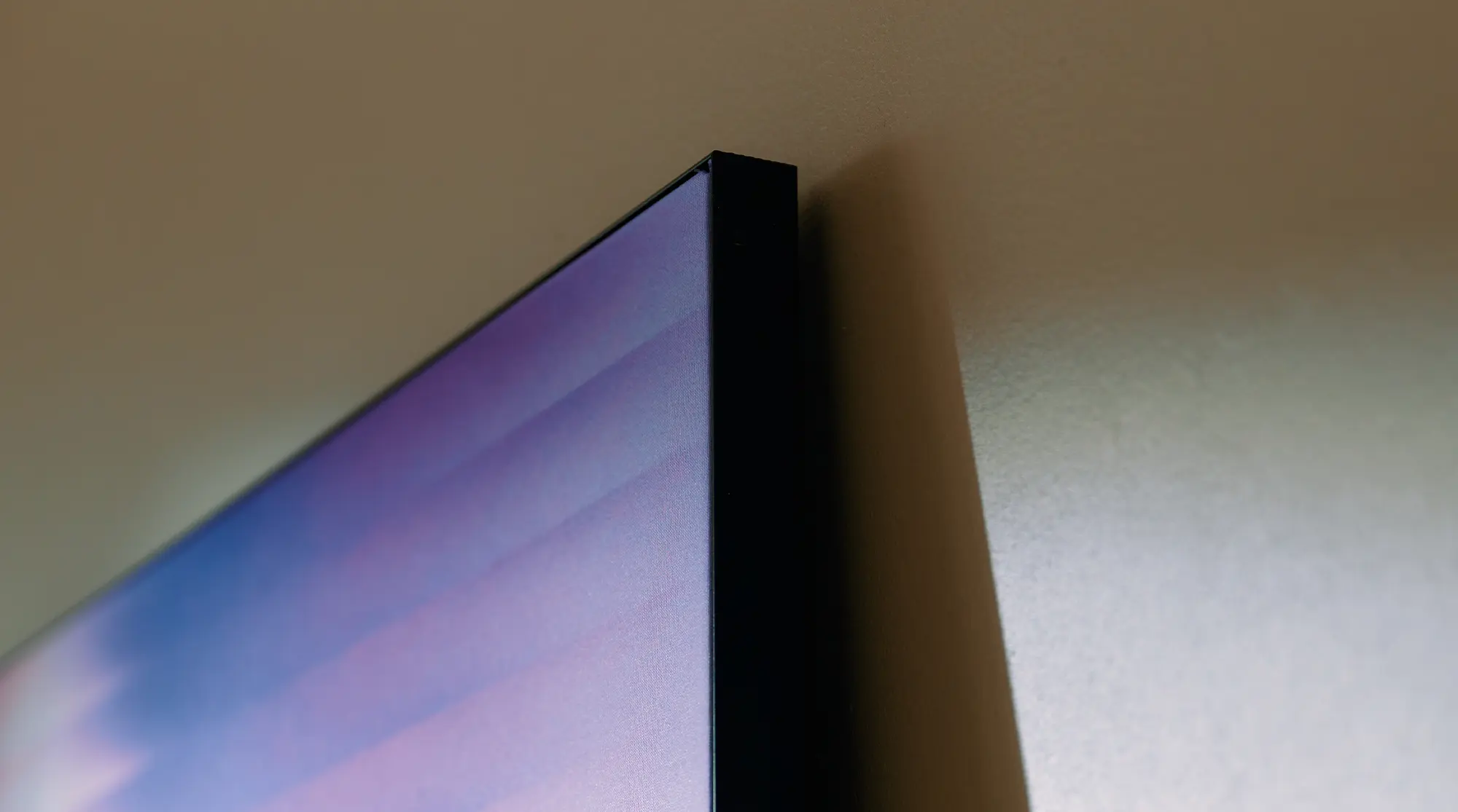 Close-up side view of a thin, flat TV mounted on a beige wall.