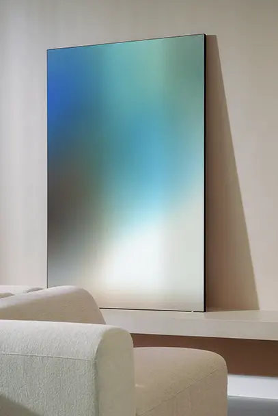Modern rectangular mirror with a blue-green gradient reflection mounted on a beige wall above a light-colored sofa.