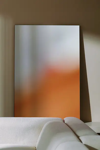 Rectangle mirror leaning against a beige wall above a white textured sofa with soft natural light casting shadows.