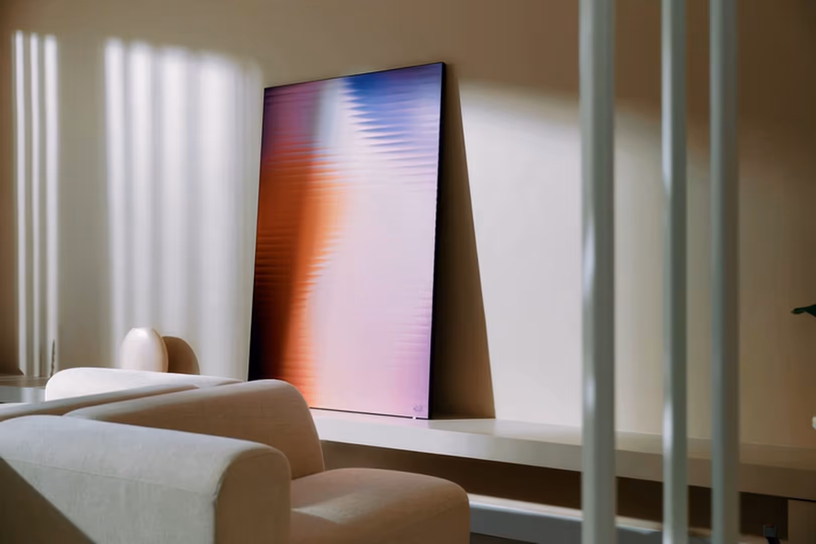 Modern beige armchair in front of a shelf holding an abstract framed artwork with gradient colors.