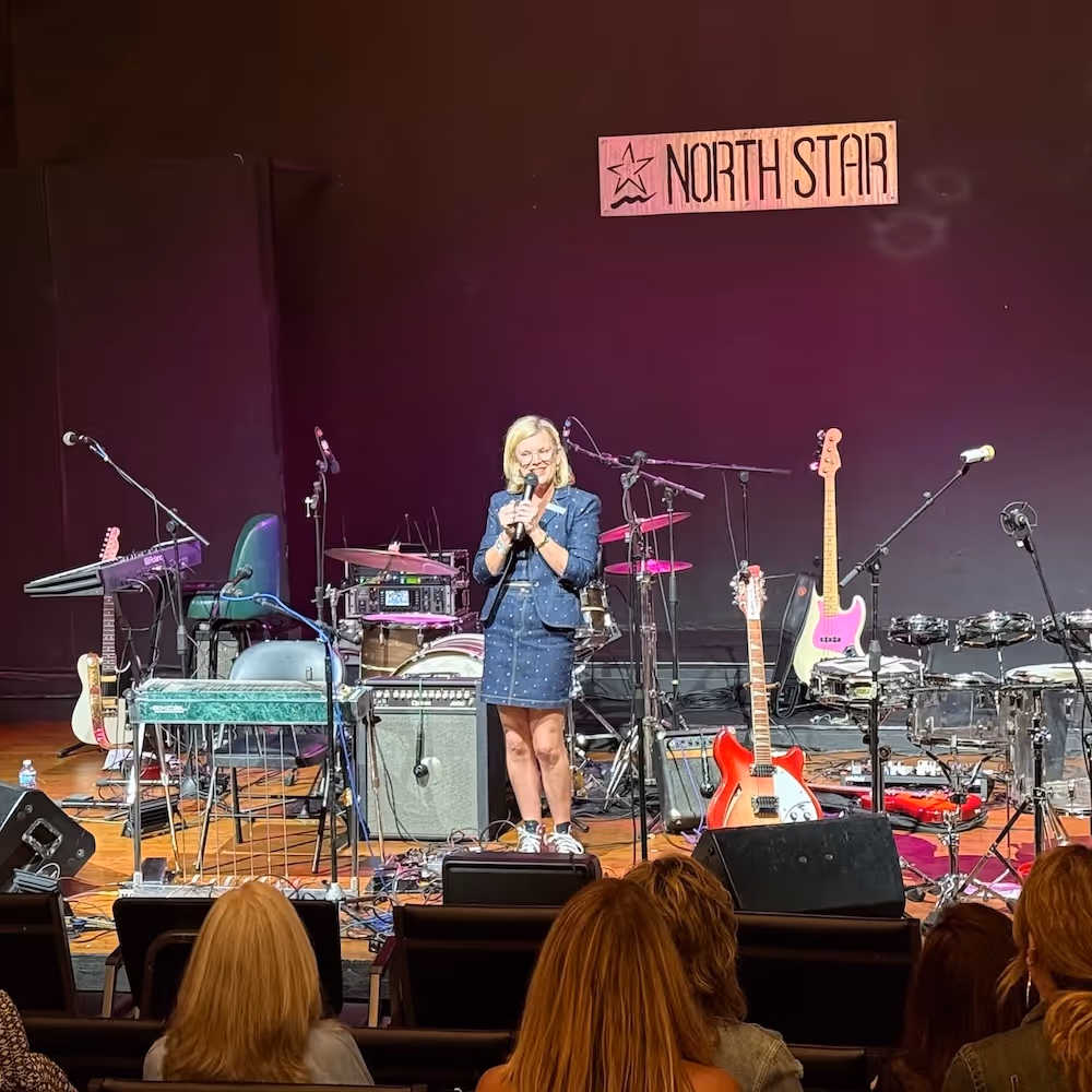 Jill Lane speaking on stage before live music at the North Star Theatre in Mandeville