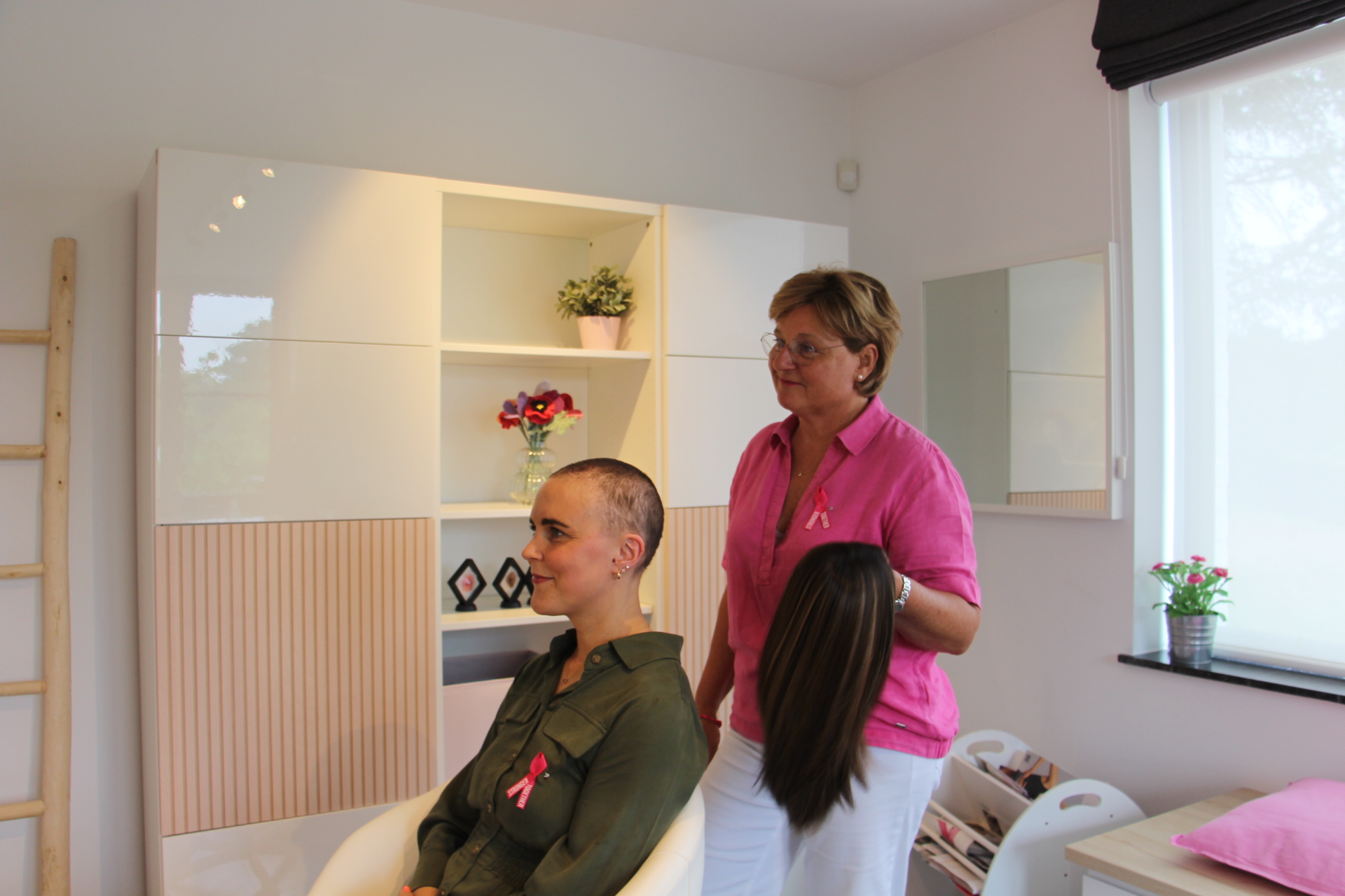 Foto van tijdens opname Nationale Loterij vrouw met afgeschoren haar + kapster heeft pruik vast