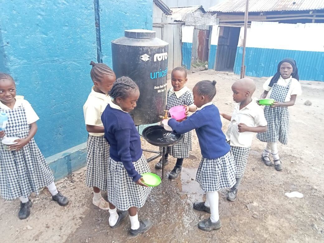 Group of young schoolchildren in uniforms washing hands at an outdoor UNICEF water station.