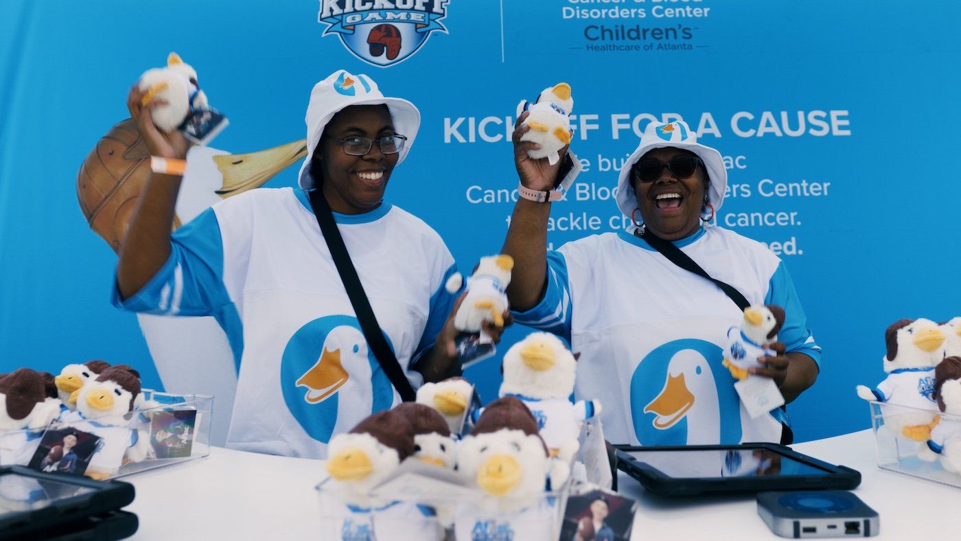 Two people holding up stuffed Aflac duck toys.