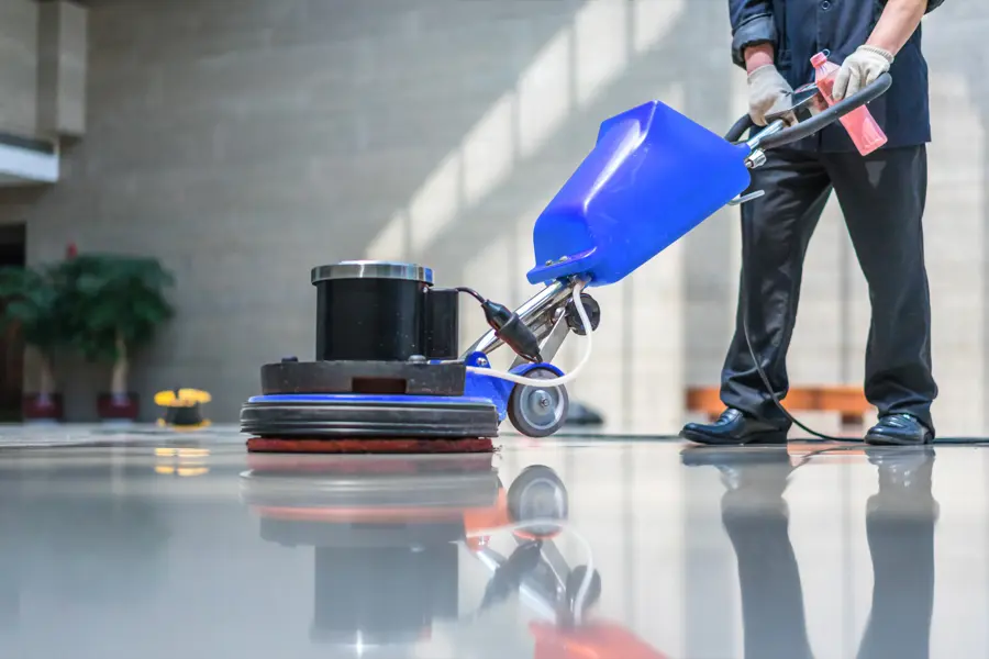 Person operating a blue floor polishing machine on a shiny, reflective surface in a spacious, well-lit room.