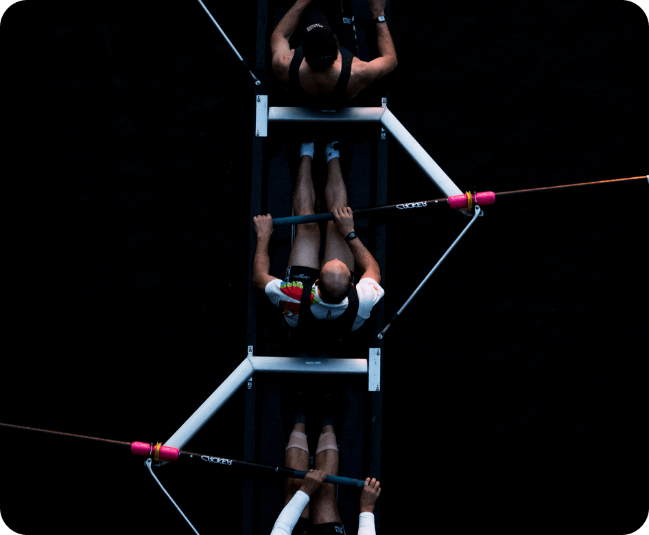 Top-down view of two rowers in a boat holding oars with dark water background.