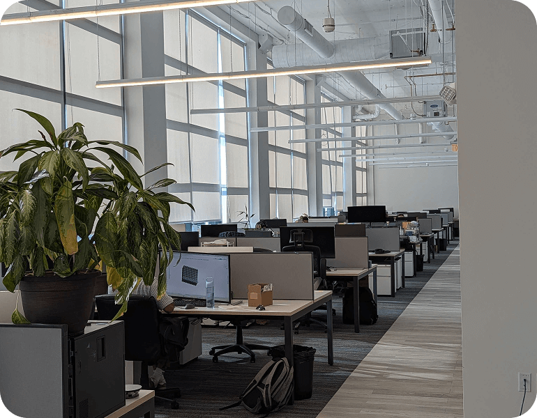 Modern GreenSight open office space with desks, computer monitors, chairs, large windows with blinds, and a large potted plant in Boston.