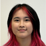 Woman with long dark hair featuring red highlights, smiling against a plain light background.