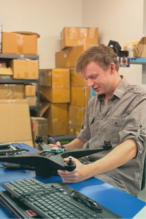 Man assembling or inspecting a drone on a blue table with cardboard boxes in the background.